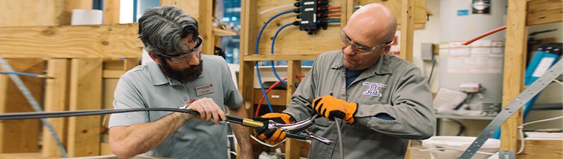 An older student and a teacher work on an electrical equipment